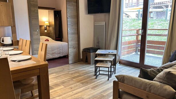 Habitación de hotel con cama, escritorio con silla, una mesita, televisor montado en la pared y puerta corrediza de vidrio que da a un área exterior.
