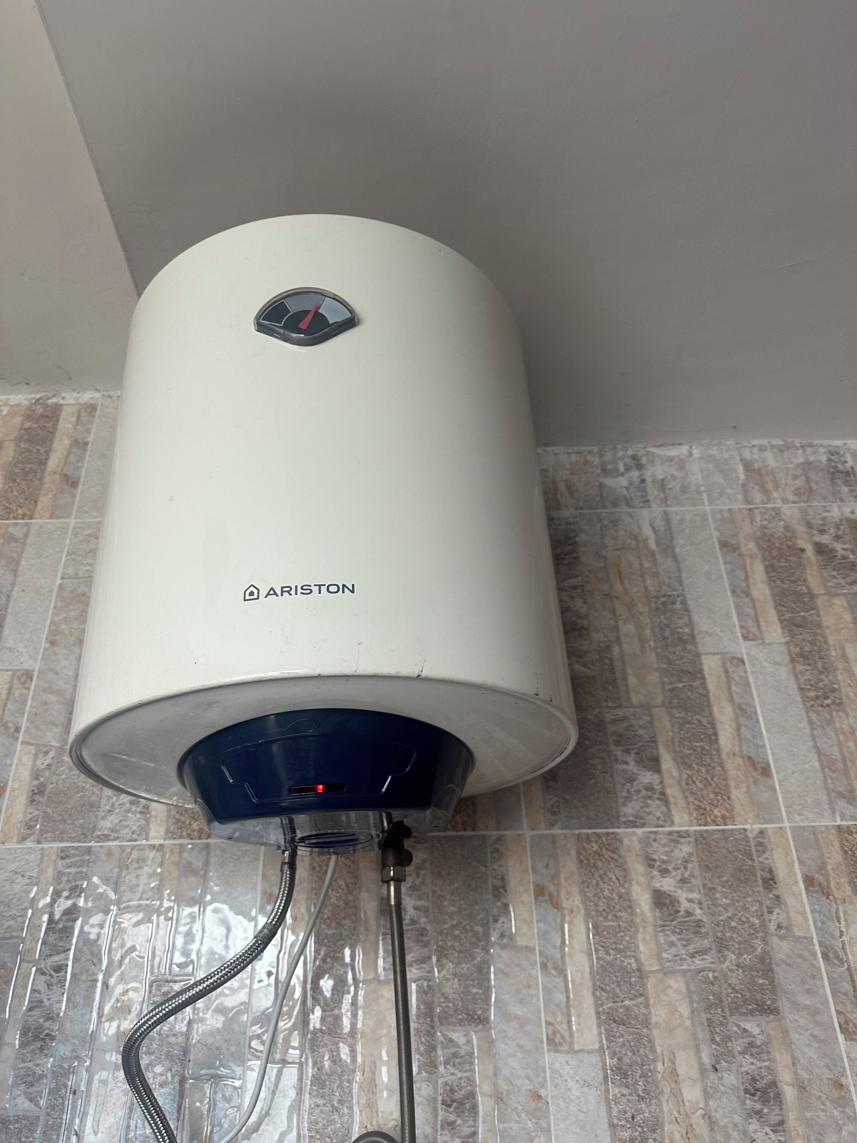 Een witte boiler met bedieningspaneel en merknaam 'ARISTON' bevestigd aan een betegelde muur.