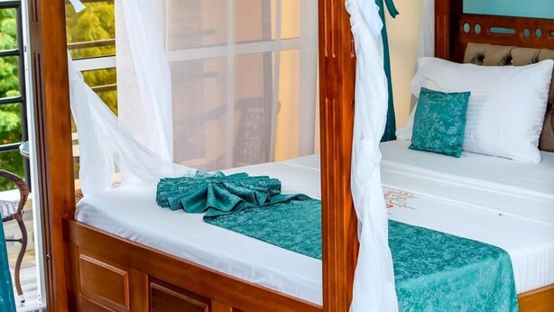 Una cama con dosel de cuatro postes, dosel blanco, cabecera de madera y colcha color aguamarina.