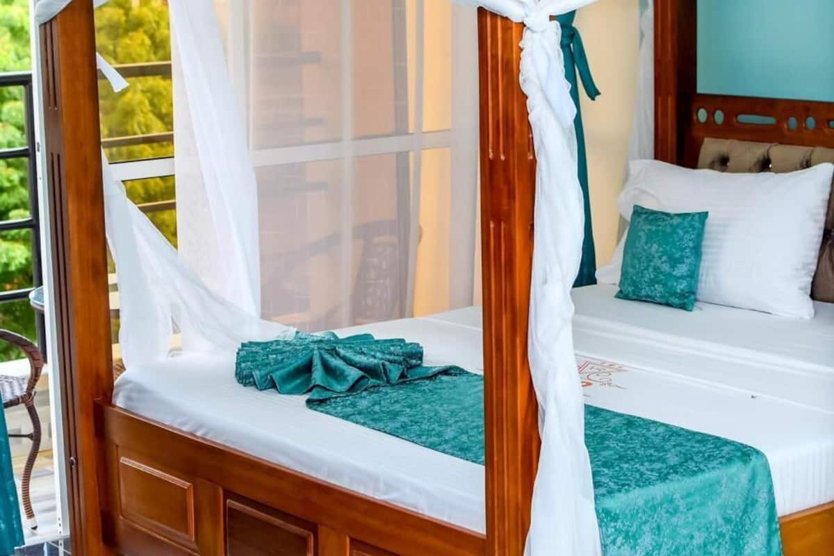 Uma cama com dossel e cortina branca, cabeceira de madeira e colcha verde-água.