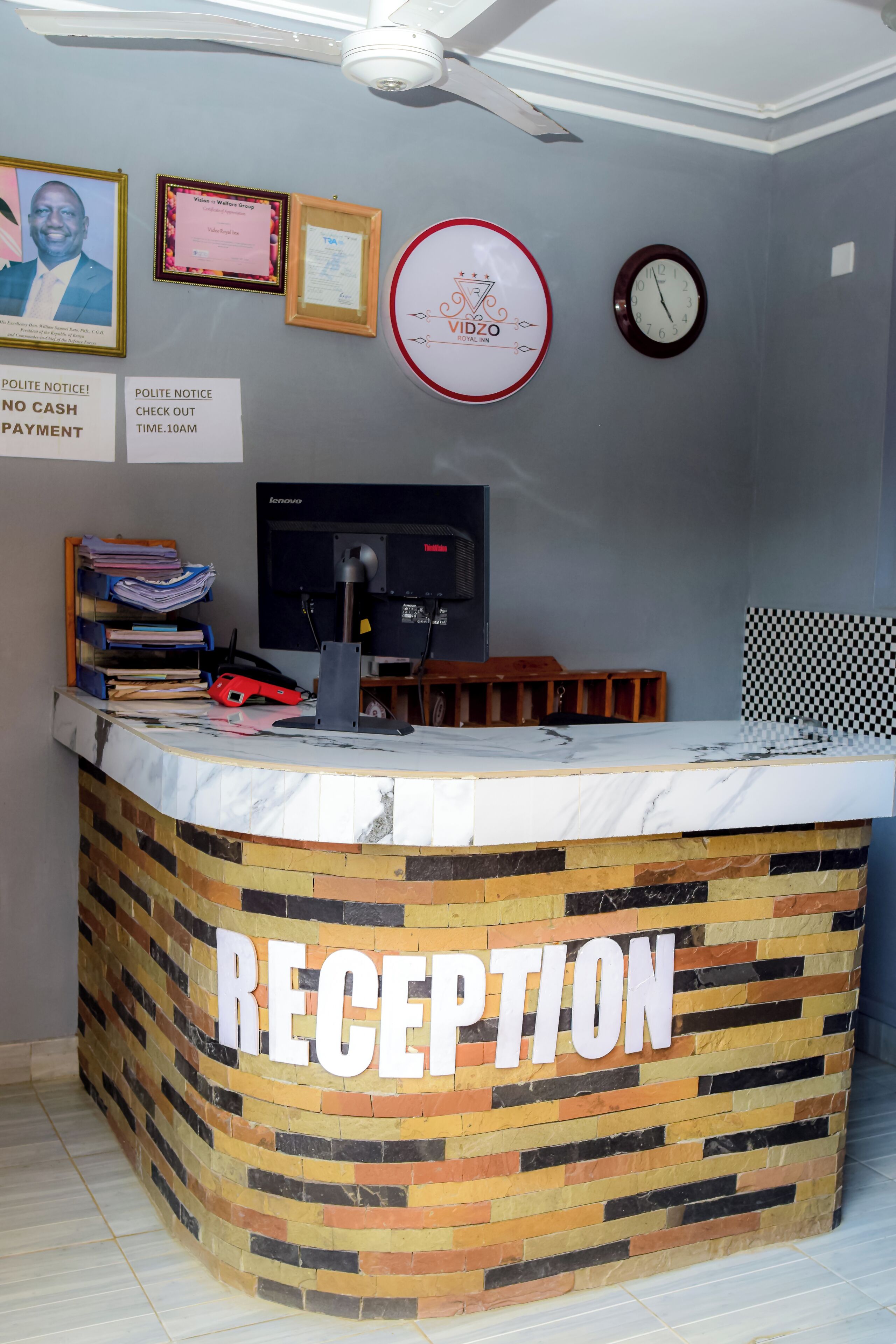 A reception area with a marble counter, a clock, framed certificates, and a check-out sign.