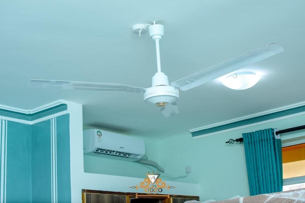 A room with teal walls, a ceiling fan, an air conditioning unit, and a window with teal curtains.