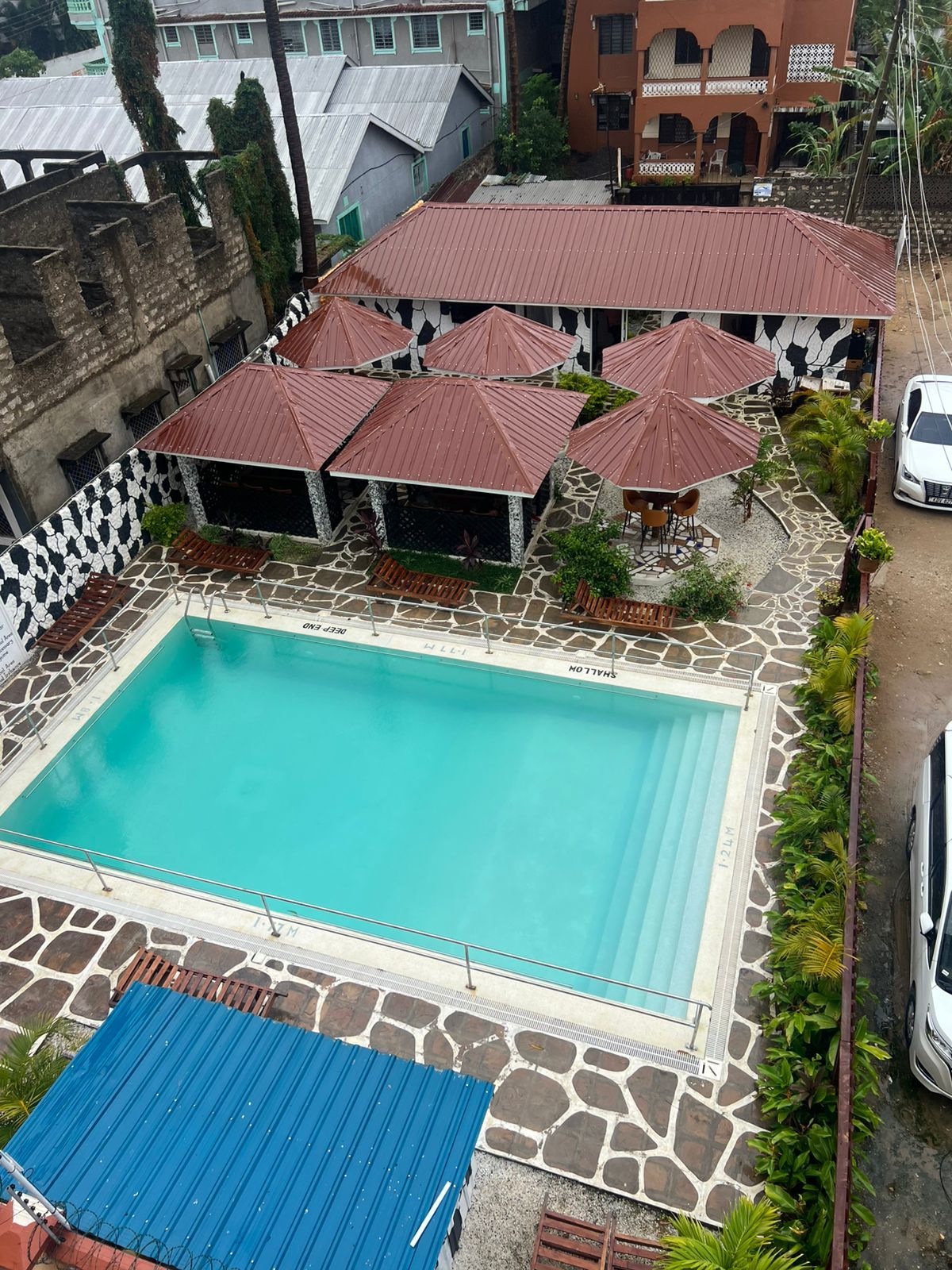 A swimming pool with a stone deck, surrounded by umbrellas and lounge chairs.