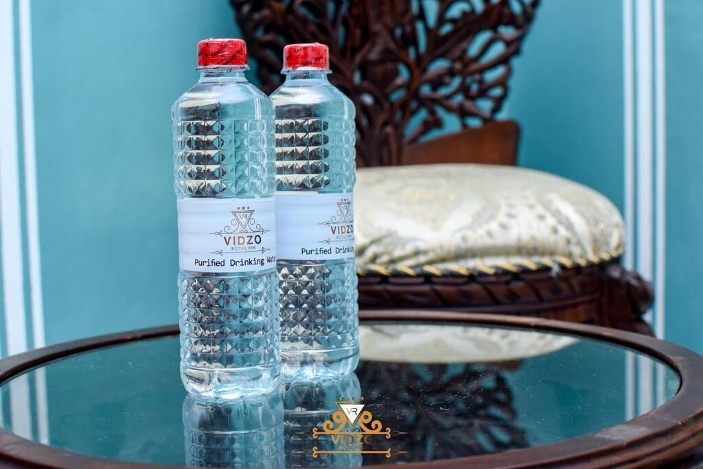 Two bottles of purified drinking water on a glass table with a decorative chair in the background.