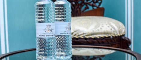 Two bottles of purified drinking water on a glass table with a decorative chair in the background.