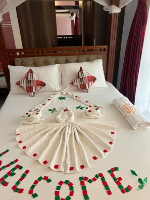 A hotel room with a large bed, two pillows, a neatly arranged towel, and a 'WELCOME' sign made of paper on the floor. - Vidzo Royal Inn  (Mtwapa)
