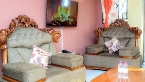 Una habitación con dos sofás tapizados con reposabrazos de madera, un televisor de pantalla plana montado en la pared y una mesa de centro de madera.