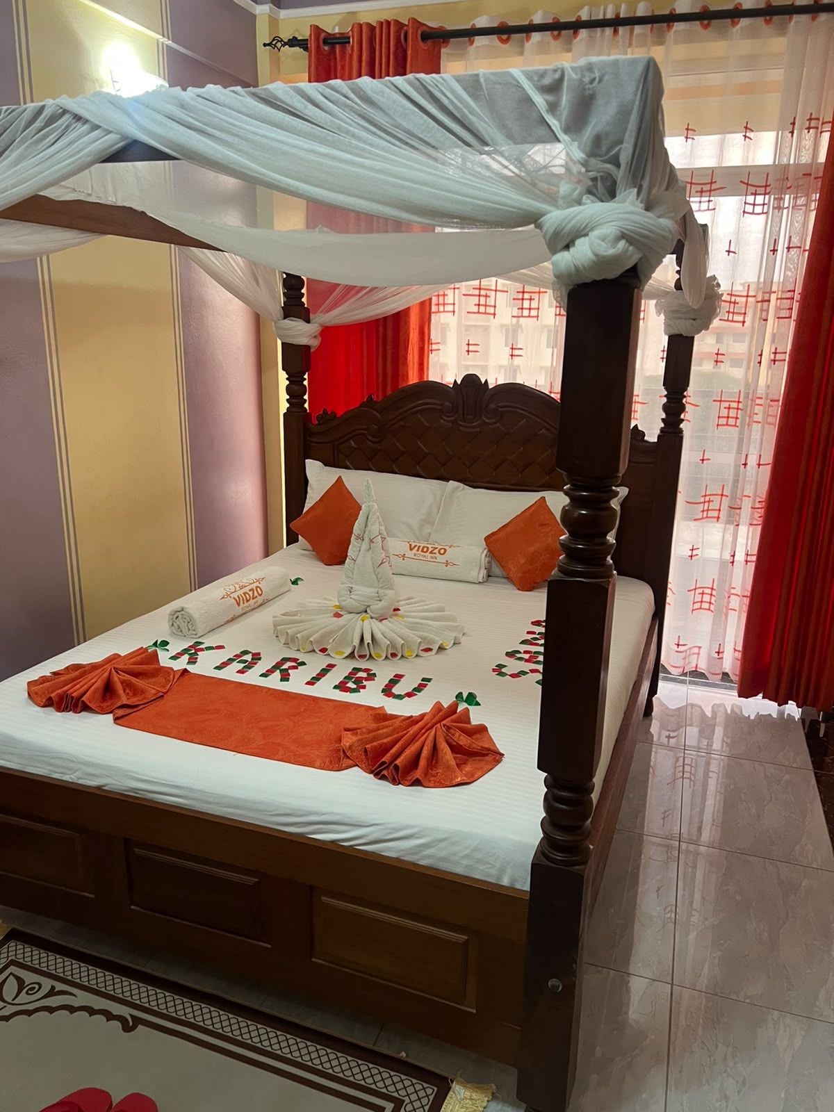 Una cama con dosel, una colcha impecable y una toalla con el nombre 'VIDZO'.