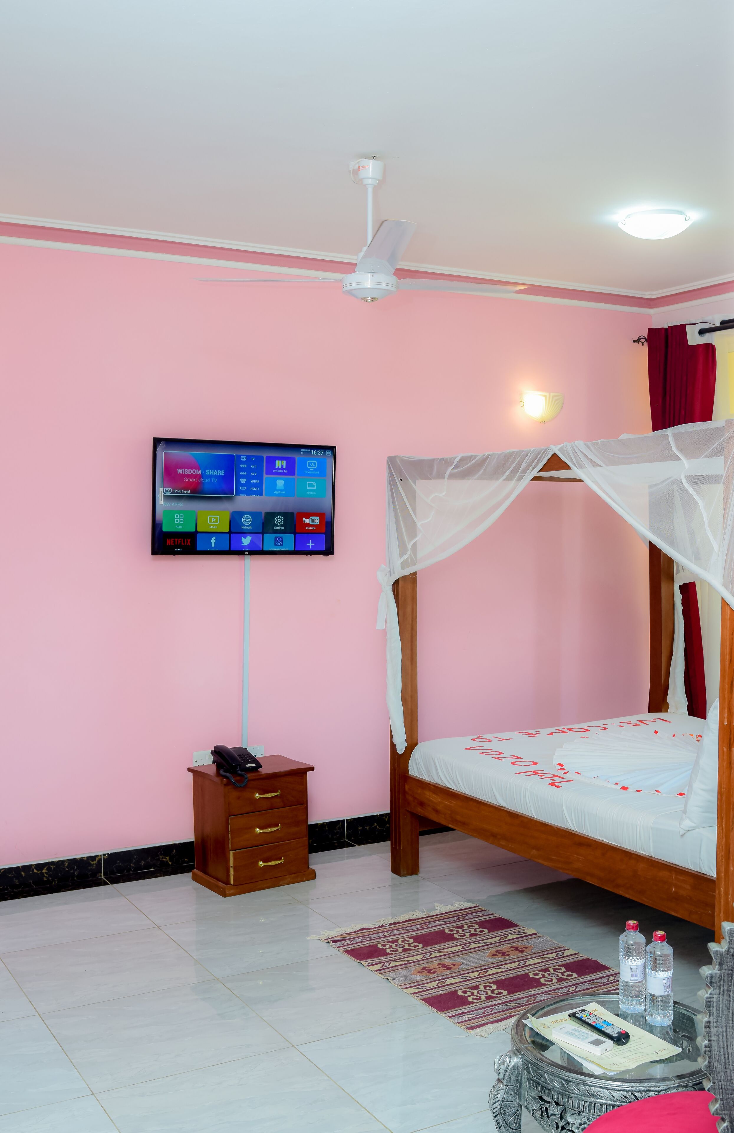 Un dormitorio con una cama, televisor montado en la pared, una mesita de noche y un ventilador de techo.