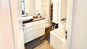 Un baño moderno con un lavabo, tocador y bañera blancos. Hay un espejo sobre el lavabo y una cortina de ducha con estampado de lunares.