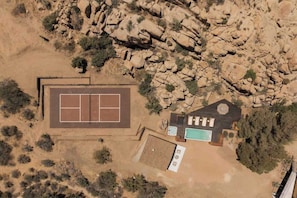 Vista aérea de una propiedad con cancha de tenis, piscina y un edificio con techo circular.