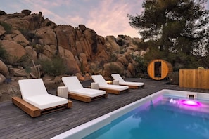 Un área de piscina con sillones de descanso, una terraza de madera y una estructura circular de madera.