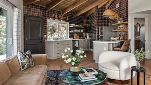 A spacious living area with a high ceiling, a kitchen with a tiled backsplash, and a dining area with a table and chairs.