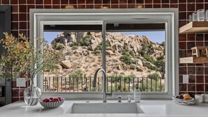 A kitchen with a large window, a sink, and a vase with flowers.