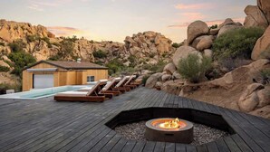 A wooden deck with lounge chairs, a fire pit, and a pool adjacent to a building with a garage.