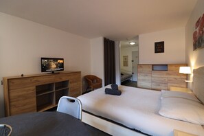 A hotel room with a bed, a desk with a television, a chair, a bedside table with a lamp, and a wall with a framed quote.