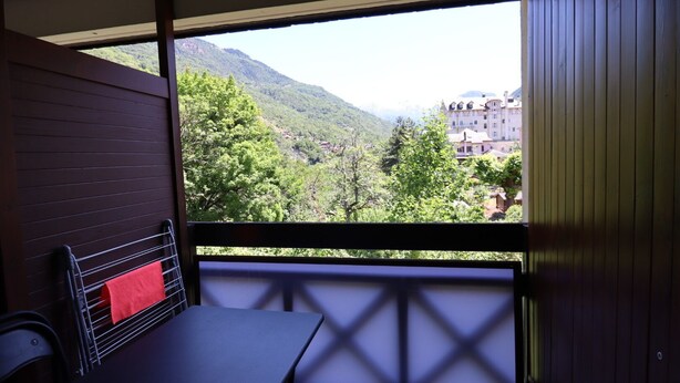 Un balcón con mesa y sillas, con vistas a un paisaje montañoso y un edificio a lo lejos.