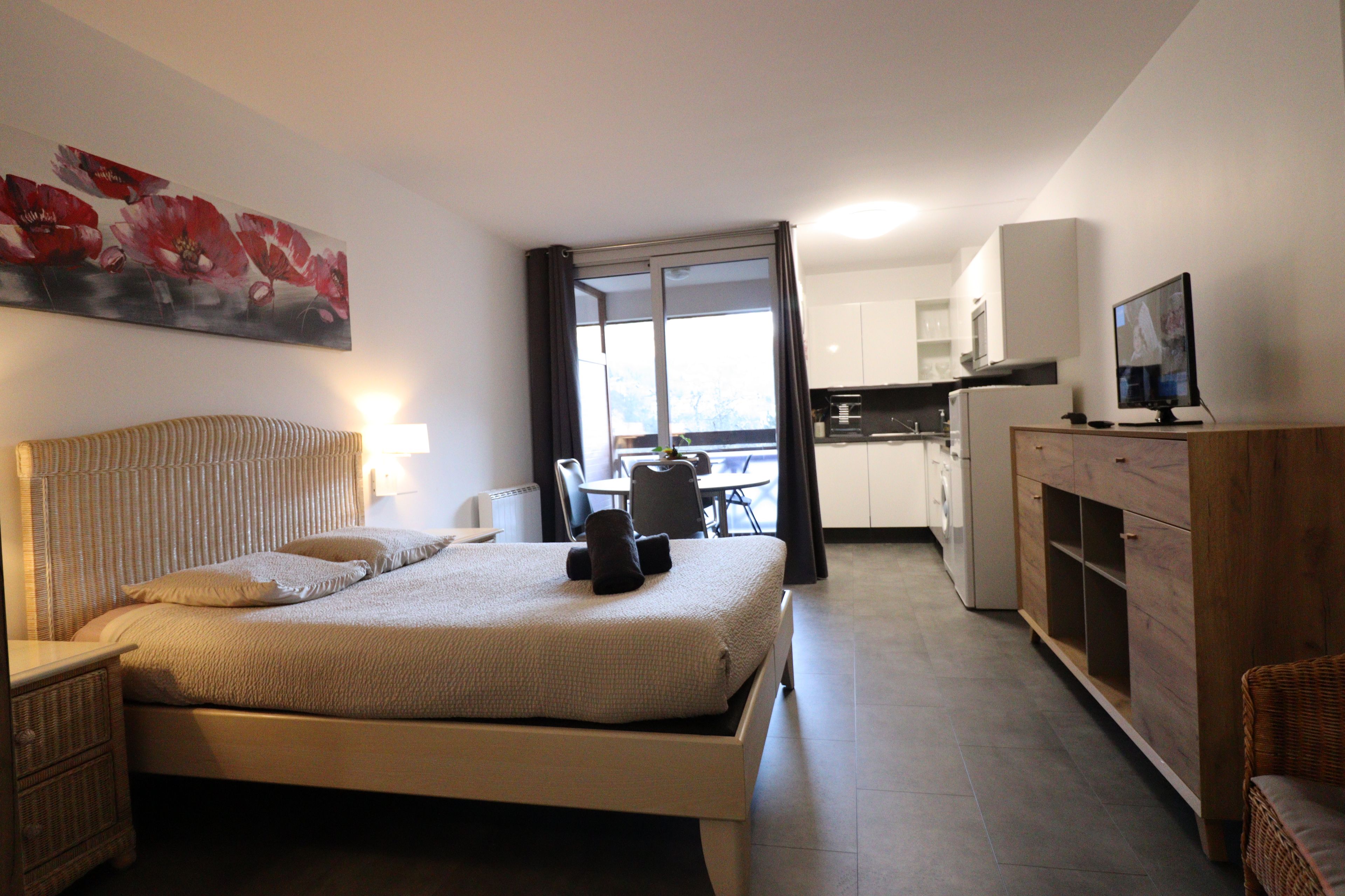 A hotel room with a bed, a television, a dining area, and a kitchen.