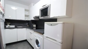 Una cocina compacta con armarios blancos, lavadora incorporada, microondas y refrigerador.