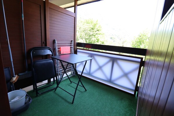 A small balcony with a table and chairs, a broom, and a trash bin.