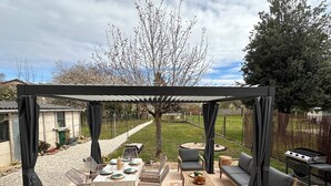 Eine Außenpatio mit überdachter Sitzgruppe, einem Esstisch für vier Personen und einem Grill.