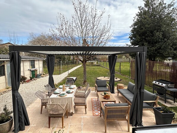 An outdoor patio with a covered seating area, a dining table set for four, and a barbecue grill.