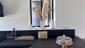 Eine moderne Küche mit schwarzem Arbeitsplatz, einem Fenster mit Ausblick und einer Vase mit Trockenblumen.