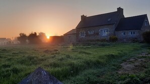 A stone house with a sloped roof, a visible chimney, and a grassy field in the foreground. - A beautiful, charming Breton home. Located in Paimpol, 1 km from the mer.Au —quiet and private. (Paimpol)