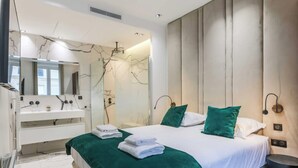 Une chambre d’hôtel moderne avec un grand lit, une coiffeuse avec un miroir et un mur en marbre.