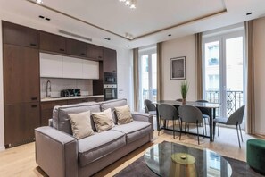 A modern living room with a grey sofa, a glass coffee table, a dining area with a table and chairs, and a kitchen with dark cabinets and appliances. - Superb AC Apartment Center of Paris (Paris)