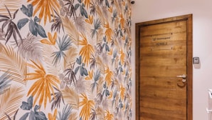 Une pièce dont le papier peint est orné de motifs de feuilles tropicales et qui possède une porte en bois portant l’inscription « Checkmyguest HOME 2 ».