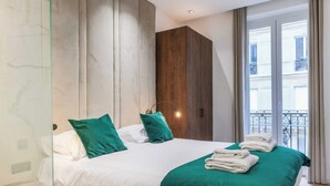 Une chambre d’hôtel moderne avec un lit, des oreillers verts, une armoire en bois et un balcon avec des rideaux.