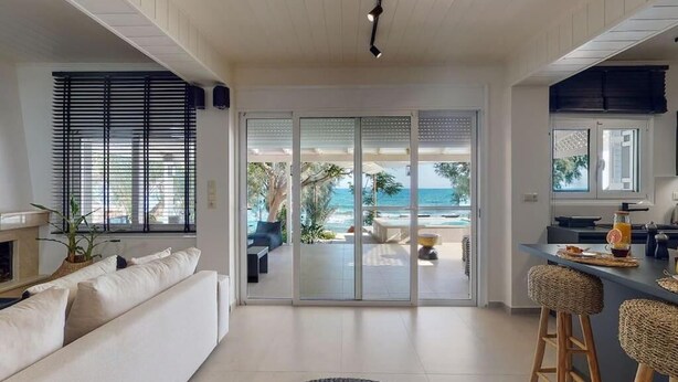 A modern living room with a sofa, a dining area with stools, and a view of the ocean through large sliding doors. - NIKKON LUXURY LIVING is a luxury private villa, in top of the sea.Enjoy LUXURY. (Viannos)