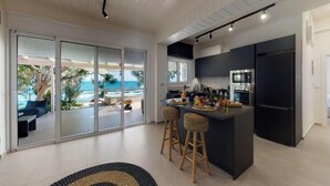 A modern kitchen with a central island, bar stools, and a view of the ocean through large sliding doors. - NIKKON LUXURY LIVING is a luxury private villa, in top of the sea.Enjoy LUXURY. (Viannos)