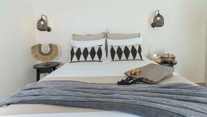 A neatly arranged bedroom with a bed, two wall-mounted lamps, a small round side table, and a decorative wall piece. - NIKKON LUXURY LIVING is a luxury private villa, in top of the sea.Enjoy LUXURY. (Viannos)