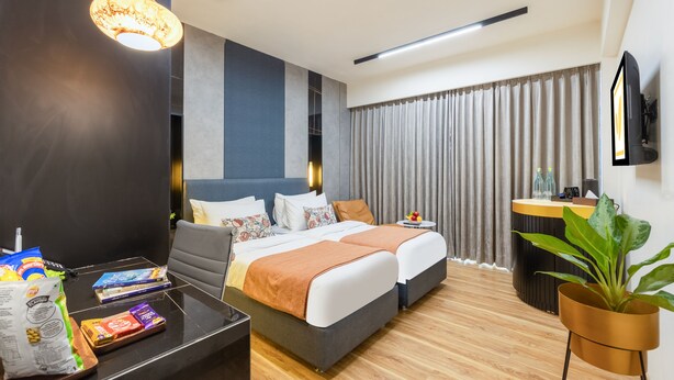 A hotel room with a modern design, featuring a large bed, a desk, a chair, a potted plant, and a television. - Hotel Limon Sector 45 Gurgaon (Gurugram)
