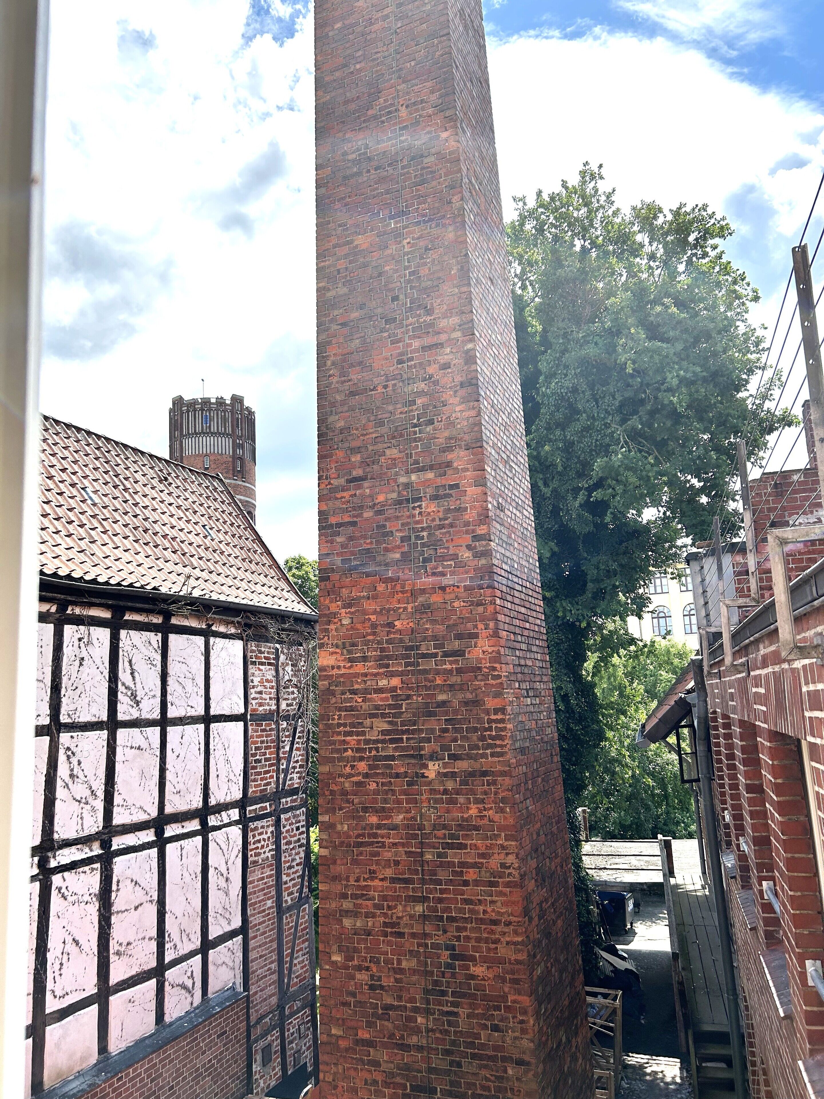 A brick chimney, a window with a grid pattern, and a tree in the background.