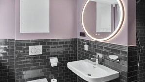 A modern bathroom with a white sink, a toilet, and a mirror with a circular light. - Apartment 2 Plum (Lüneburg)