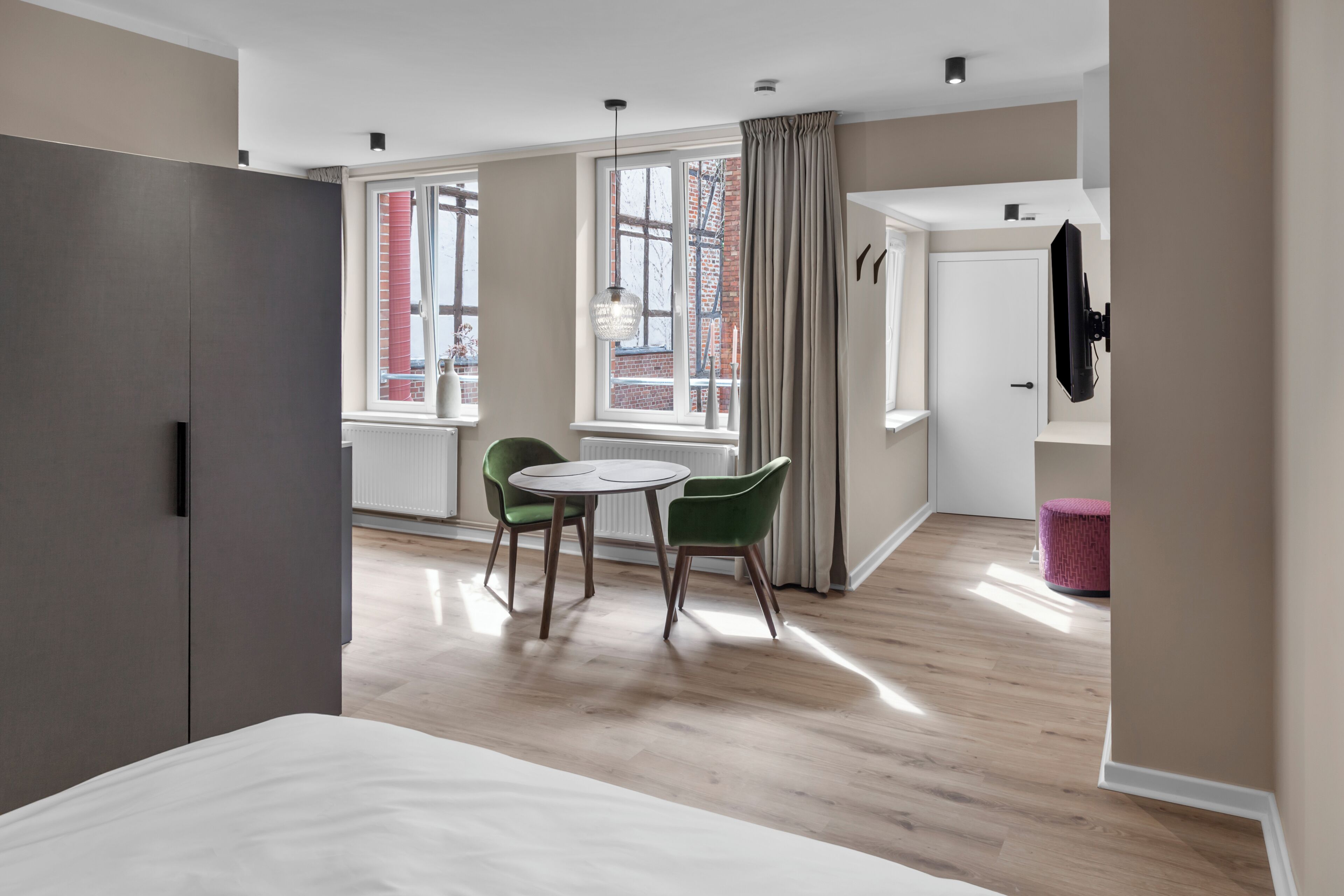 Ein modernes Hotelzimmer mit einem Bett, einer Essecke mit zwei Stühlen, einem Tisch und einem Vorhangfenster.
