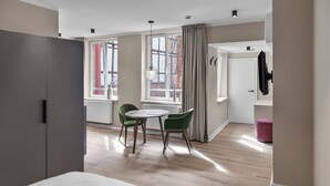 A modern hotel room with a bed, a dining area with two chairs, a table, and a window with curtains. - Apartment 2 Plum (Lüneburg)