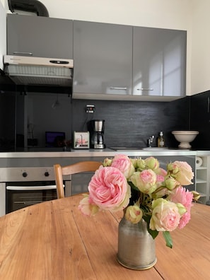 A kitchen with grey cabinets, a coffee maker, and a vase with flowers on a wooden table. - Léonie's house - 2 bedrooms - private courtyard - wifi (Châteauroux)