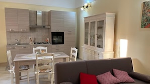 A modern kitchen with light wood cabinets, a dining table with chairs, and a built-in oven. There is a white cabinet with glass doors to the right. - CASA ROSALBA Typical southern house with vaulted roof a few miles from the beautiful (Taranto)