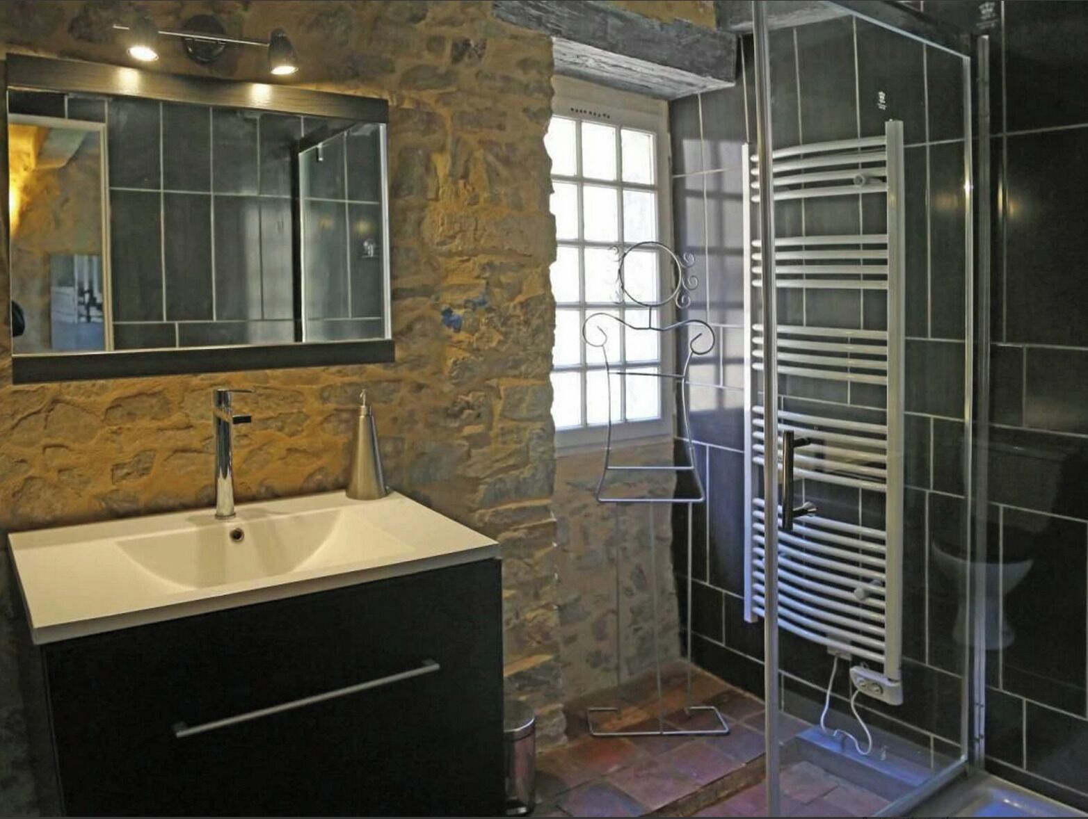 A bathroom with a stone wall, a white sink, a mirror, and a glass shower enclosure.