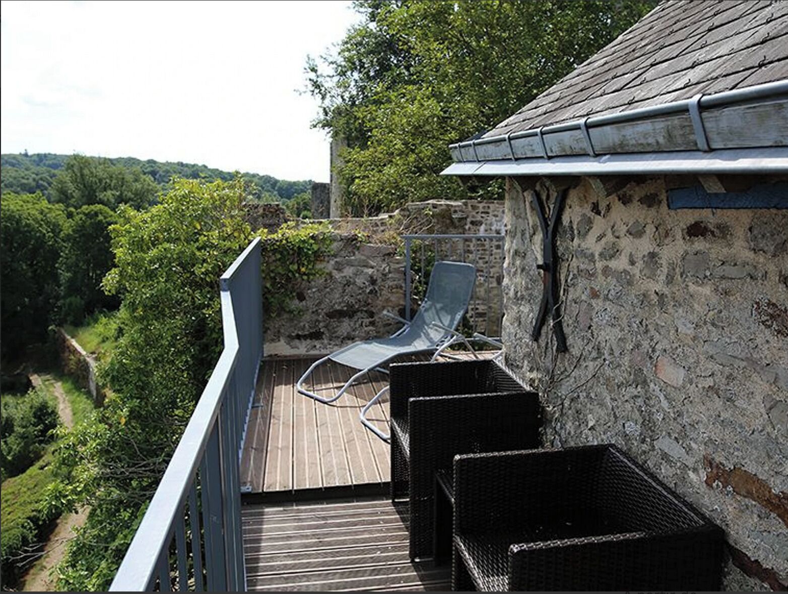 Un balcon doté de meubles en osier et offrant une vue sur une vallée boisée.