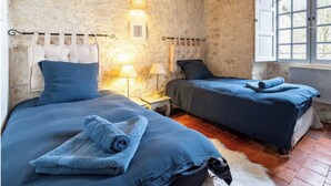 A room with two beds, each with a headboard, a small window, and a wall-mounted light fixture.