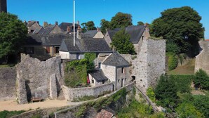 A historic stone castle with a prominent tower, surrounded by lush greenery and traditional buildings.