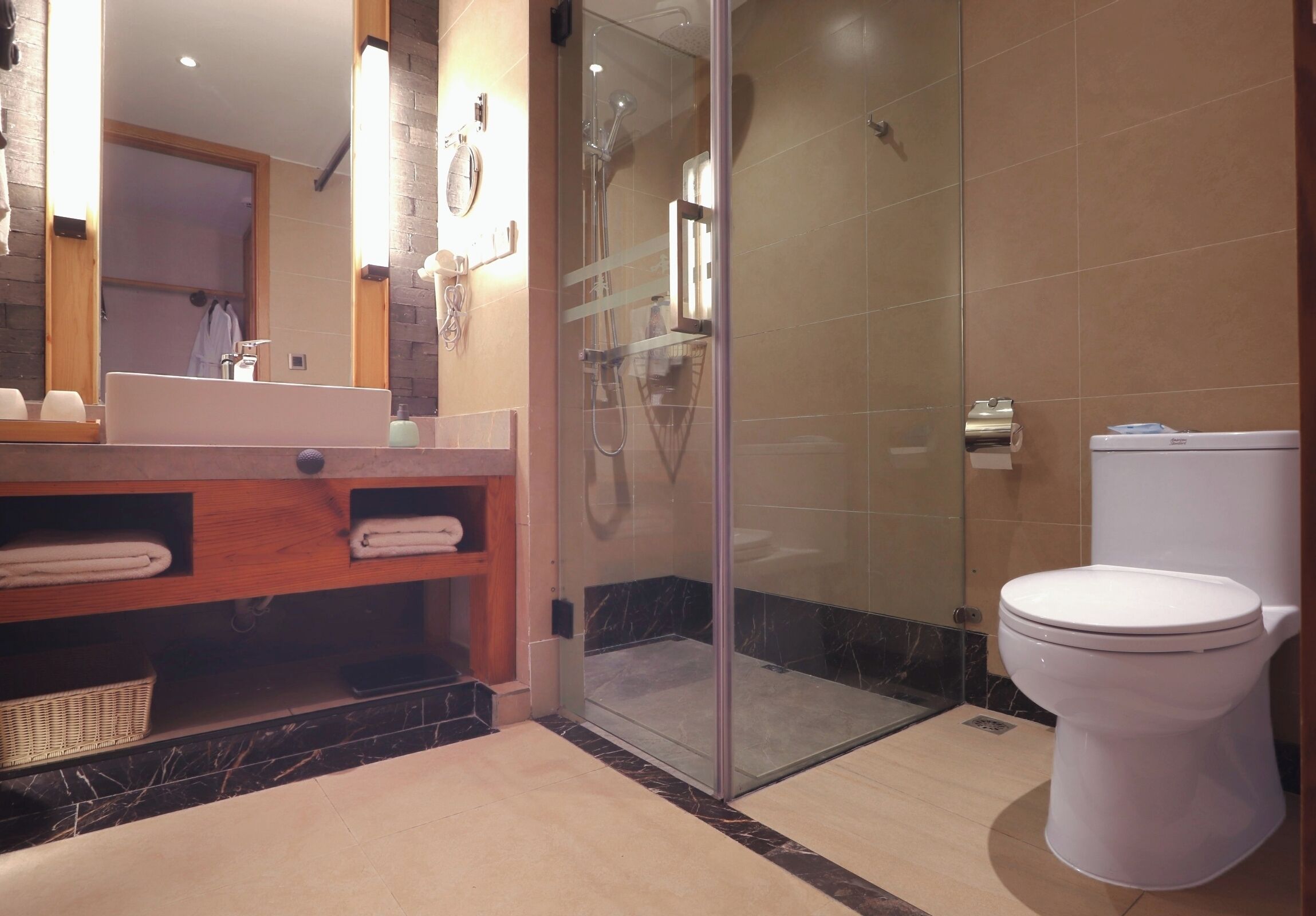 A modern bathroom with a glass-enclosed shower, a white toilet, and a wooden vanity with a mirror.