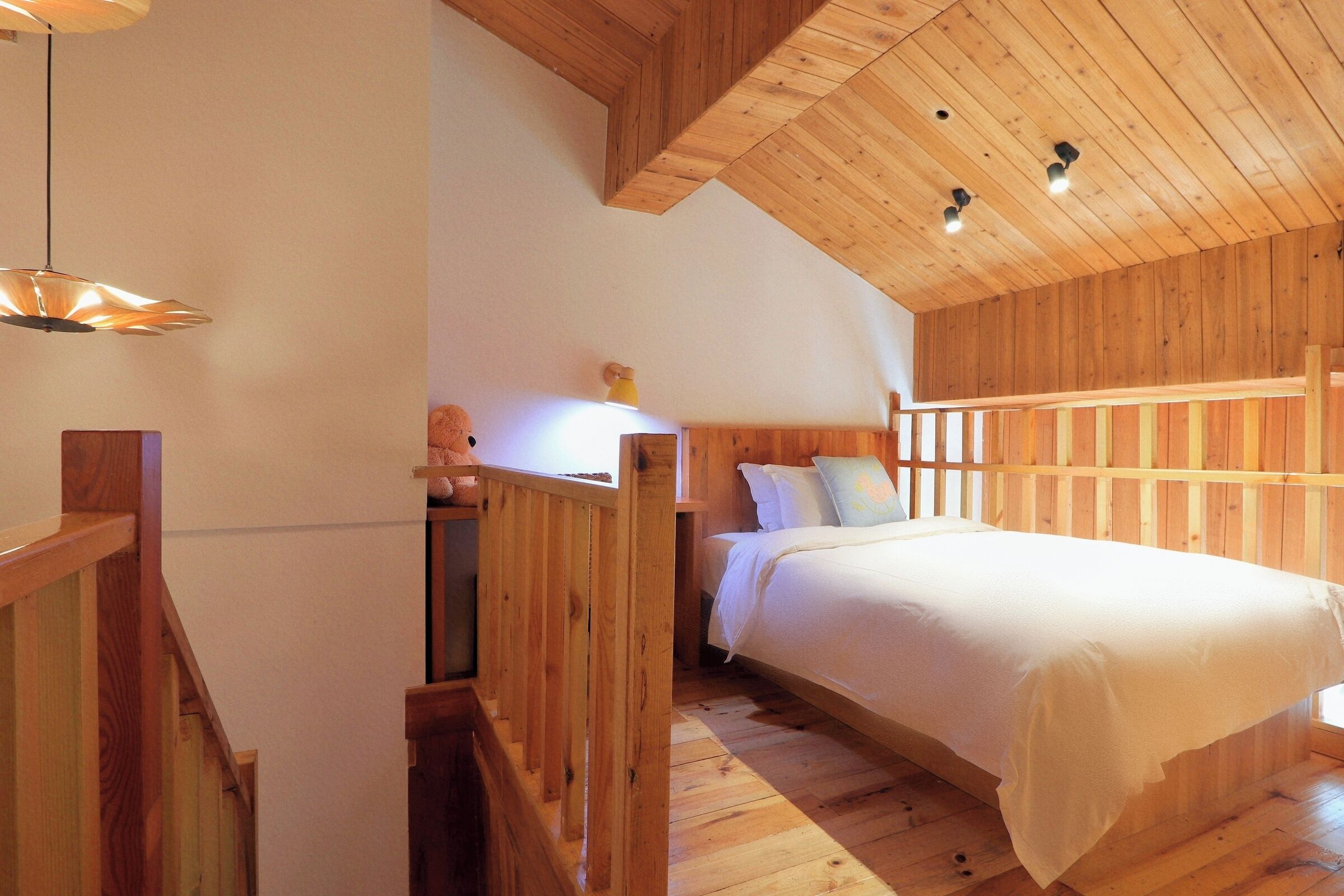 Una habitación con piso de madera, una cama, una mesita de noche y una lámpara.