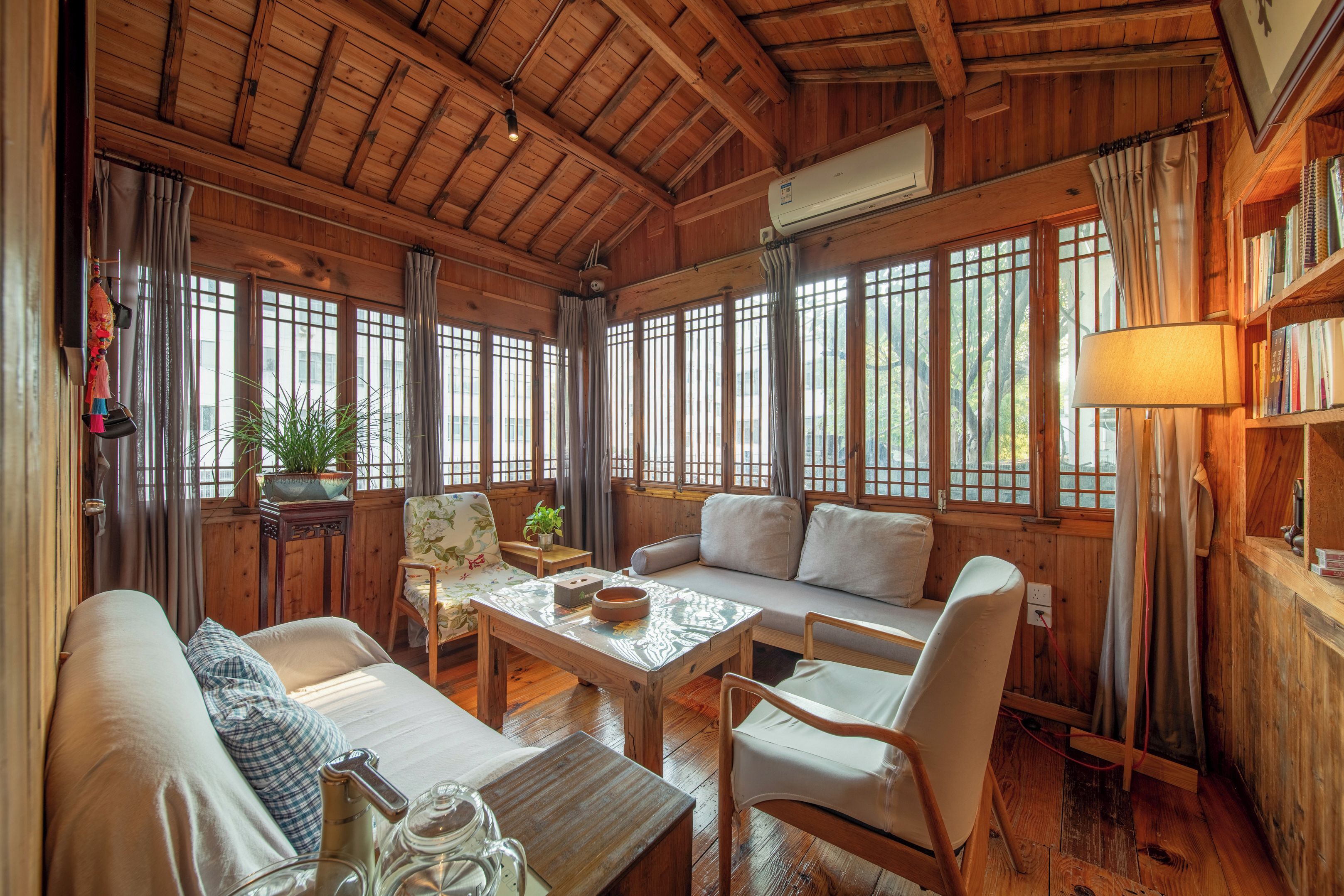 A cozy room with wooden walls and ceiling, a sofa, chairs, a table, and a bookshelf.