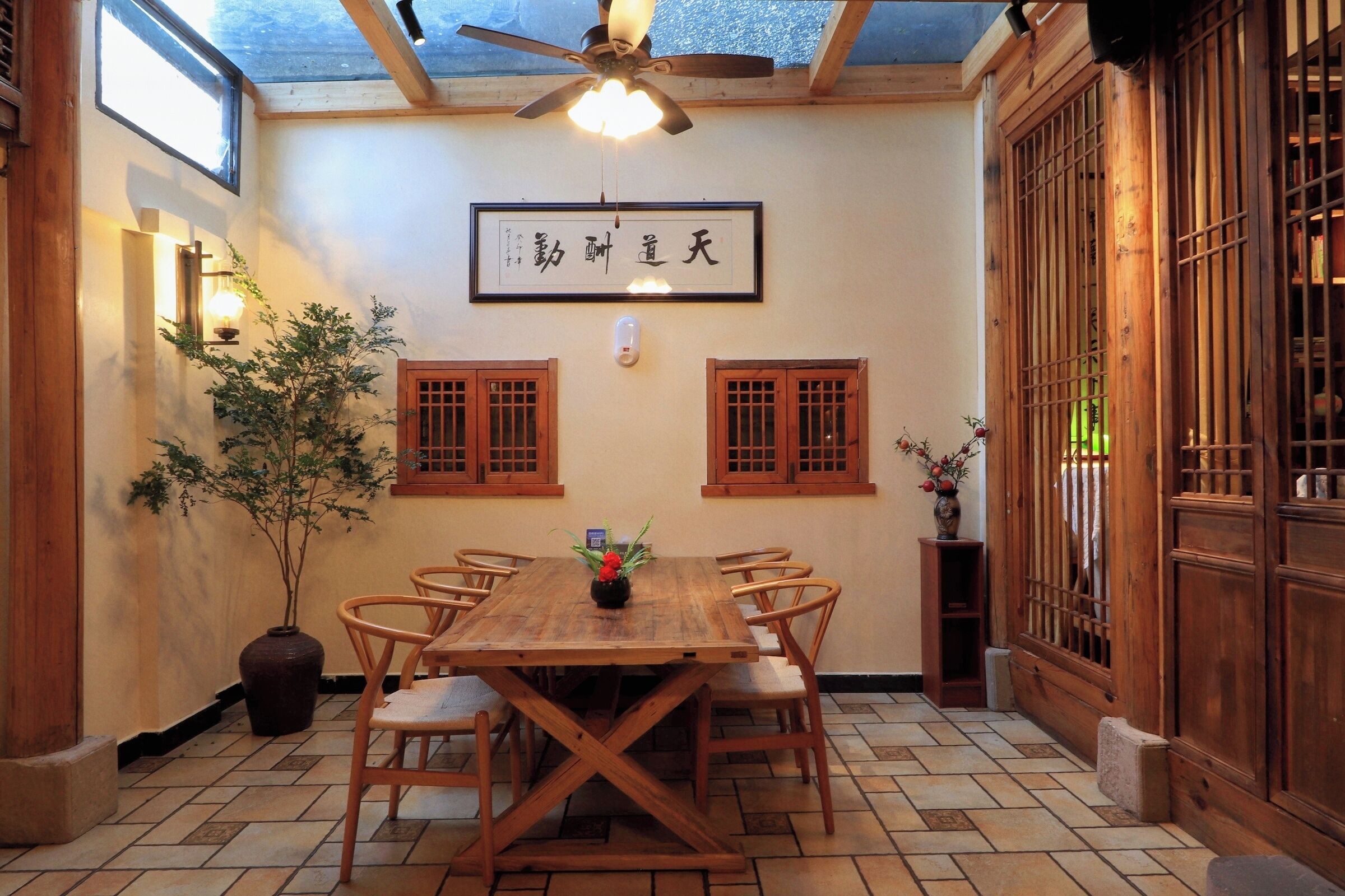 Een traditionele Japanse kamer met een houten eettafel, stoelen, een plafondventilator en een bord met Japanse tekens.
